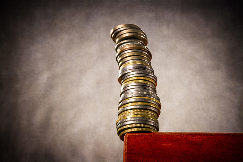 A high stack of coins stands at a table edge and threatens to crash. | usage worldwide